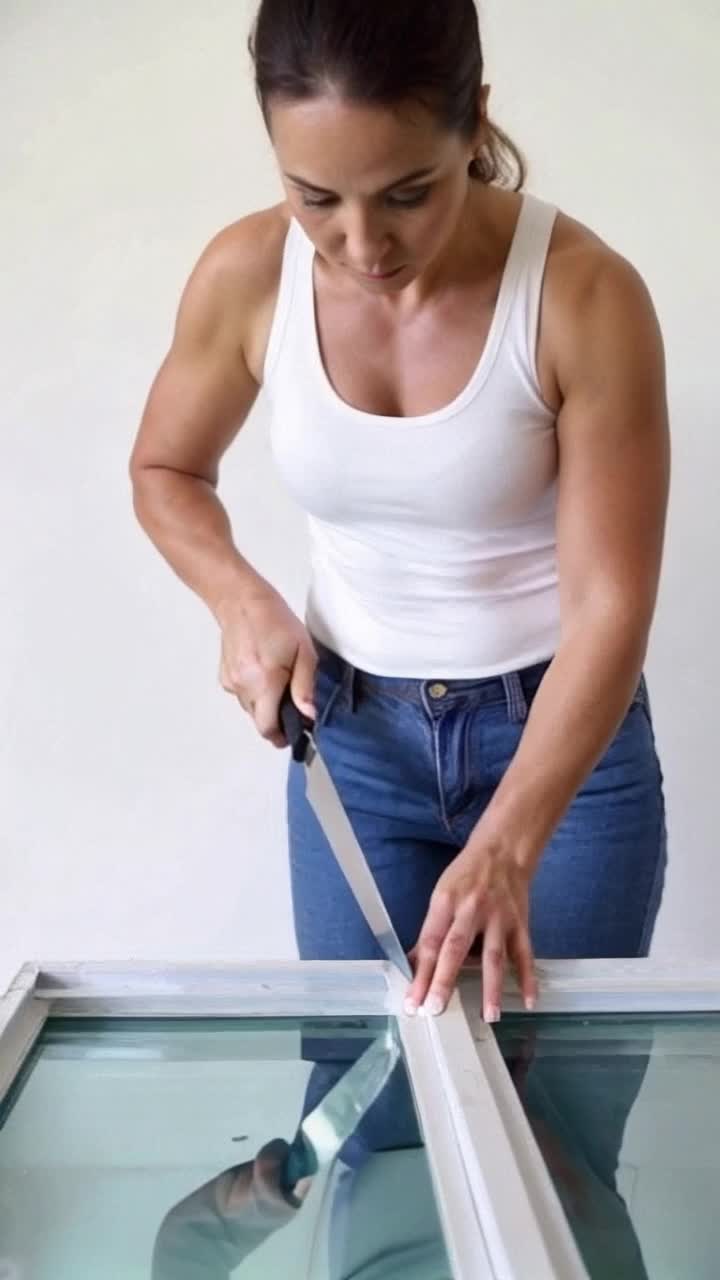 A thick panel of plexiglass is being cut diagonally with a very sharp Rambo style knife by a cute muscular woman