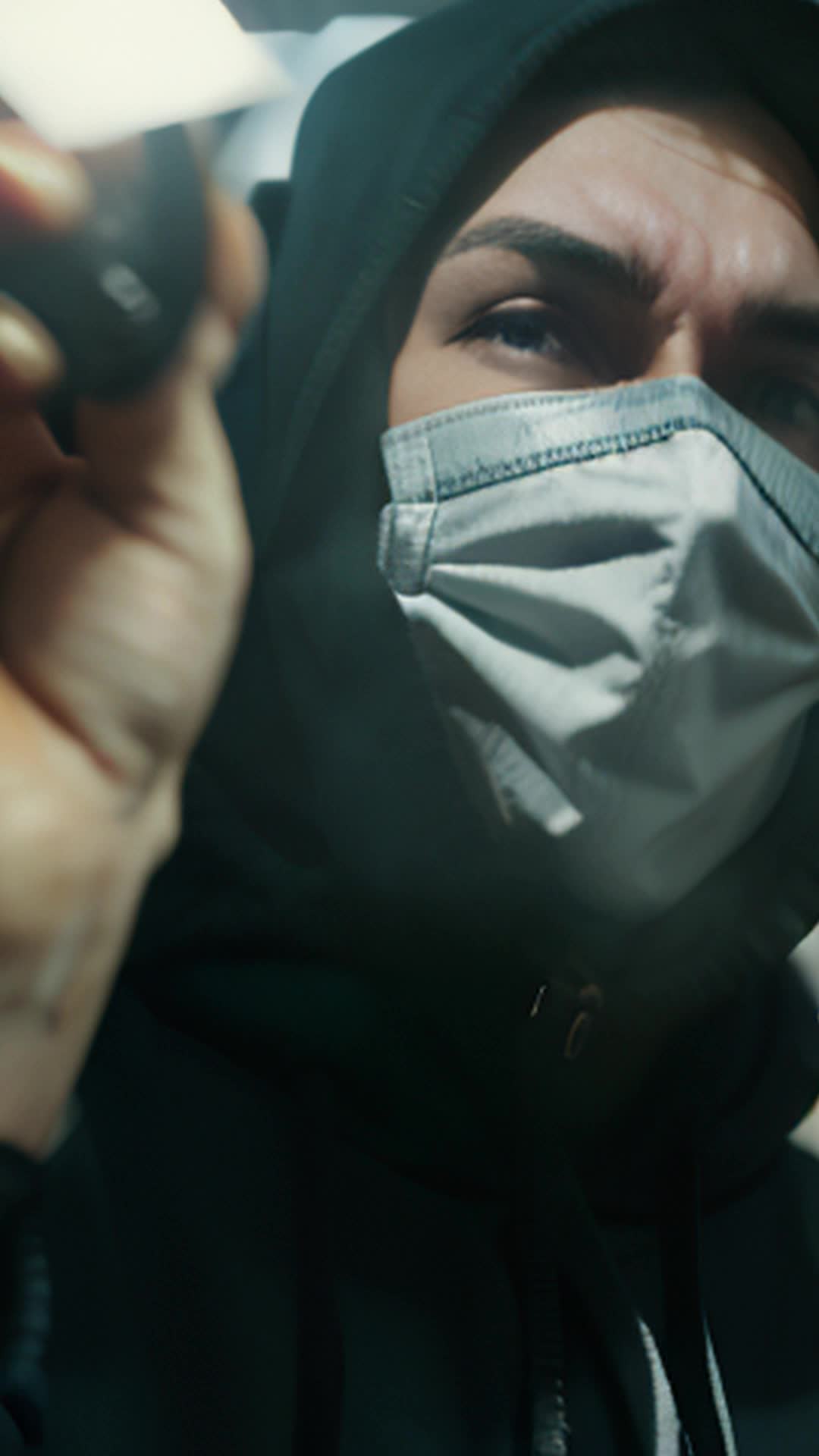 Mysterious person, black hoodie, white mask, slow walk, picks up microphone, dimly lit room, dramatic shadows, moody atmosphere, closeup of hand reaching microphone, suspenseful, steady camera angle, cinematic focus, detailed and sharp, tensionfilled moment