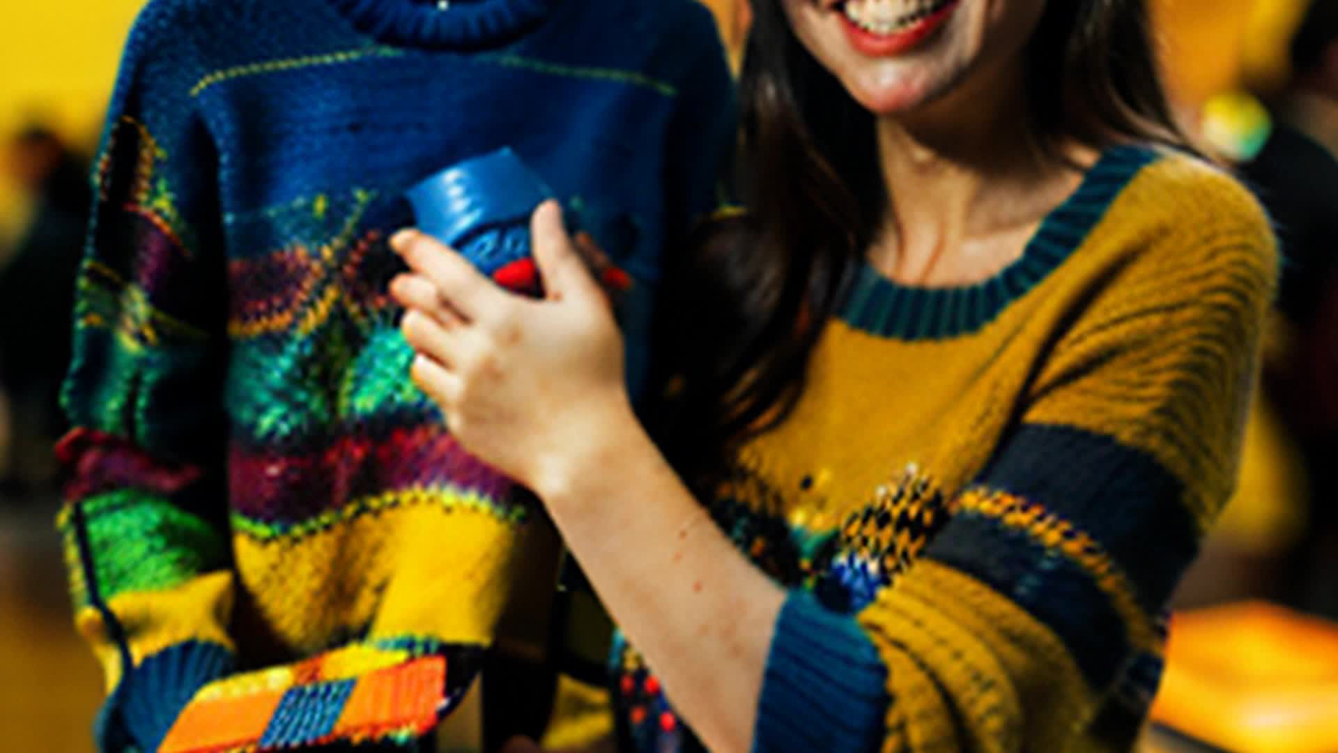 Proud Jamie displaying dazzling DIY sweater masterpiece eyeing potential buyers considering perfect gift wide angle colorful craft fair