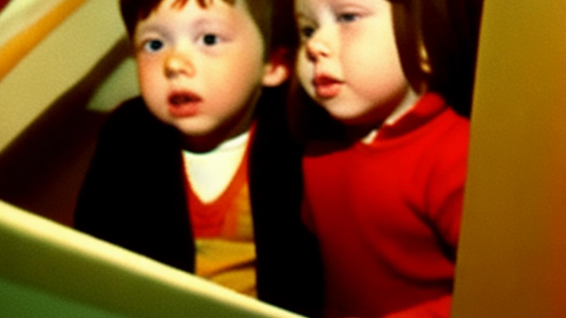 a little brunette girl and 2 brunette toddler boys spying from the staircase