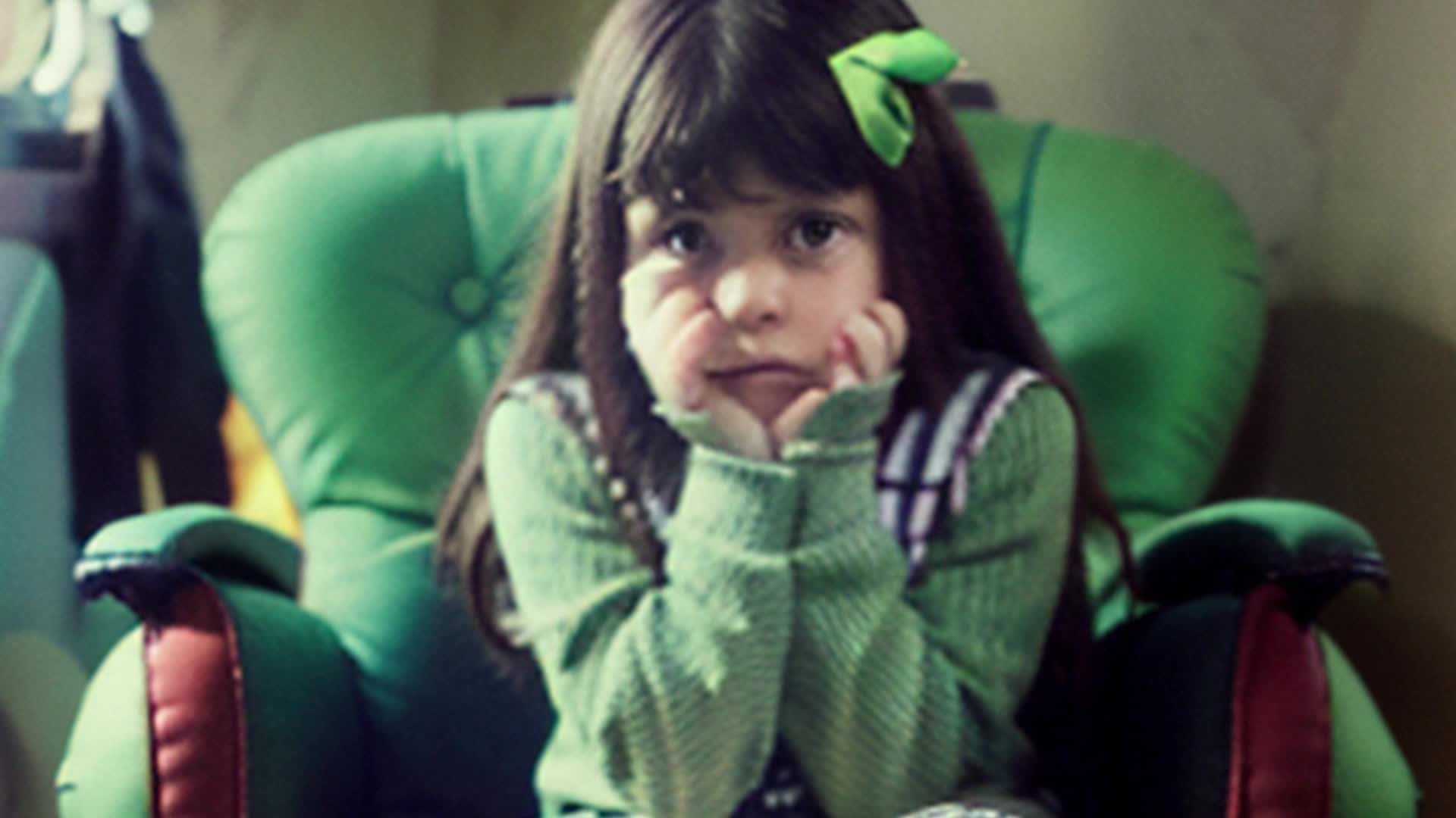 sad little girl sitting in a pink chair