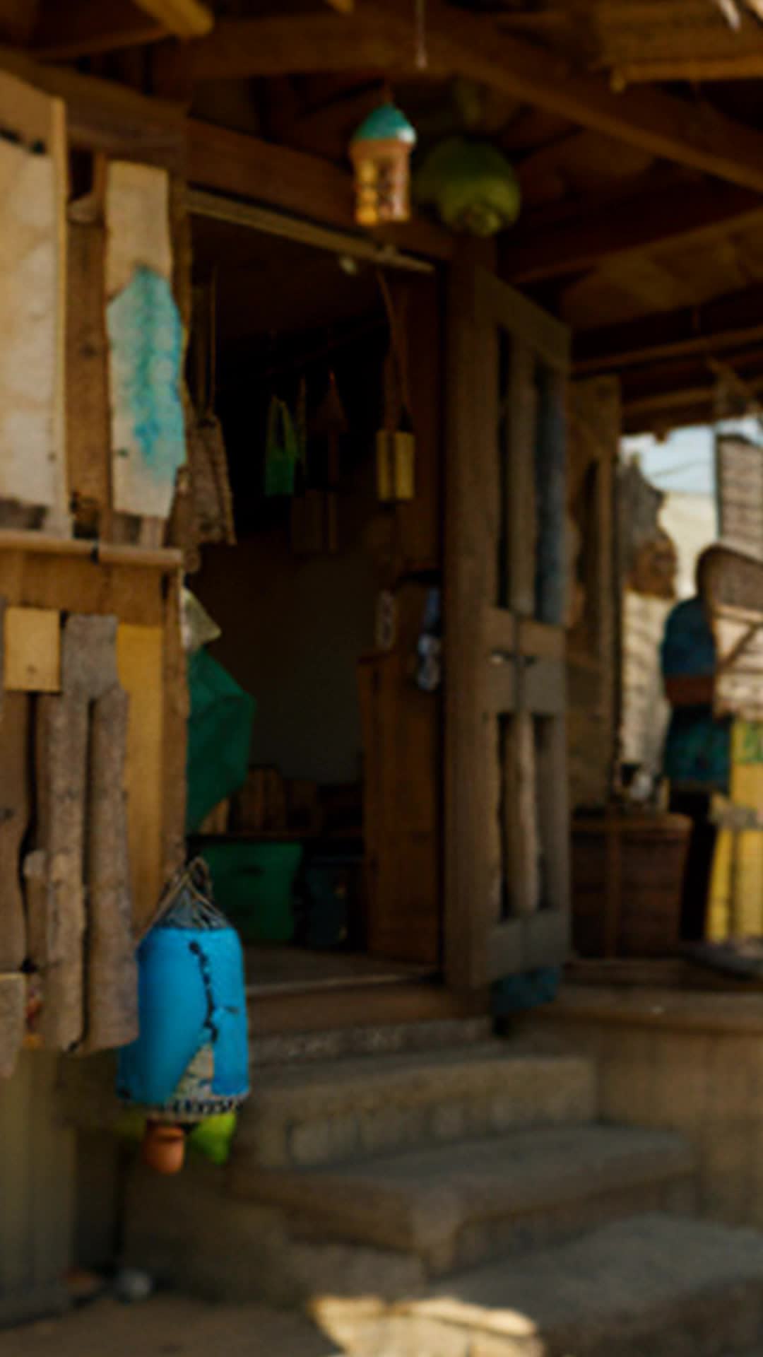 Group of actors parade through makeshift town steps resonating with harmonic clang of wind chimes close up rustic makeshift buildings colorful wind chimes hanging from every corner