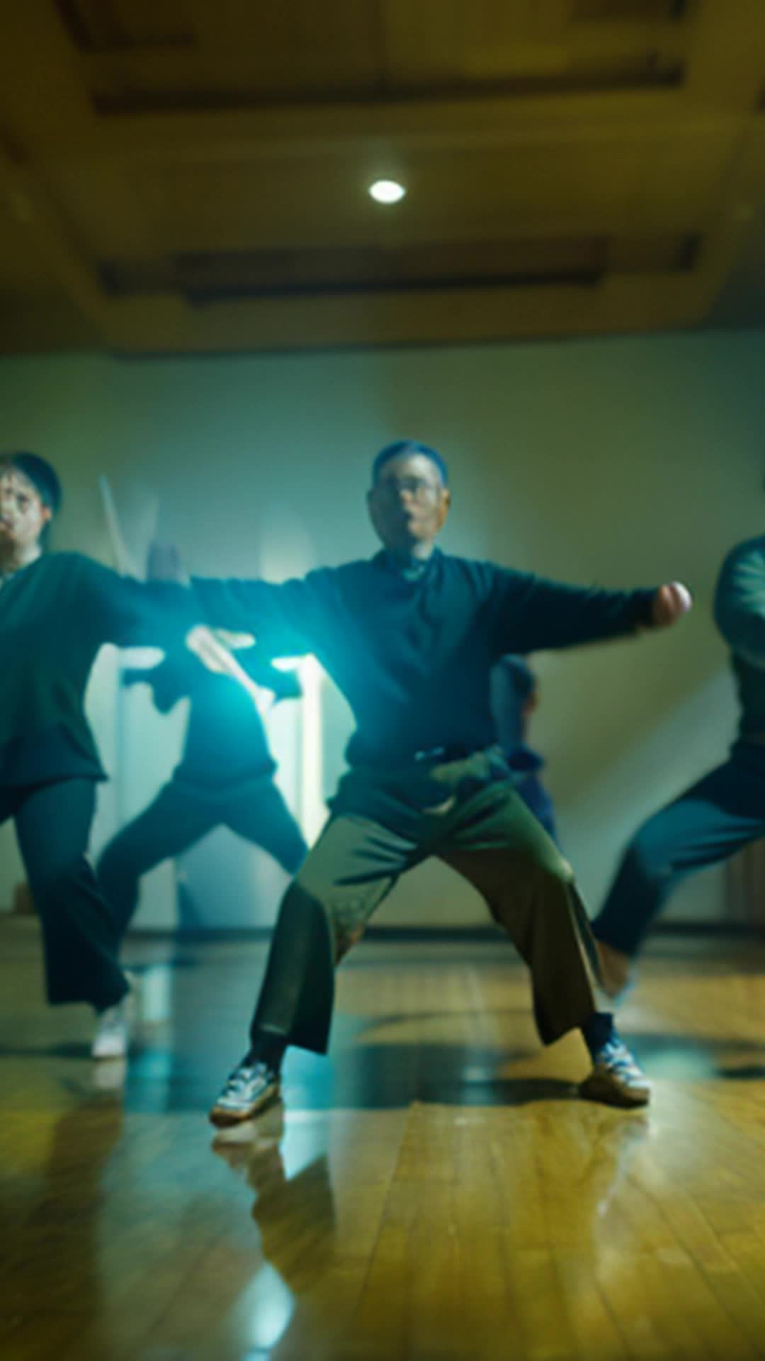 Group of dissenters performing Tai Chi Maya joins mimicking movements wide angle dimly lit spacious room