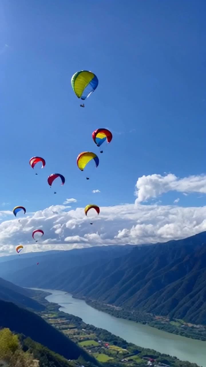 Colorful parachutes soaring gracefully through azure skies   gliding through warm currents of wind   breathtaking mountainous landscape dotted with lush green valleys and sparkling rivers below   sundrenched peaks casting playful shadows on the ground