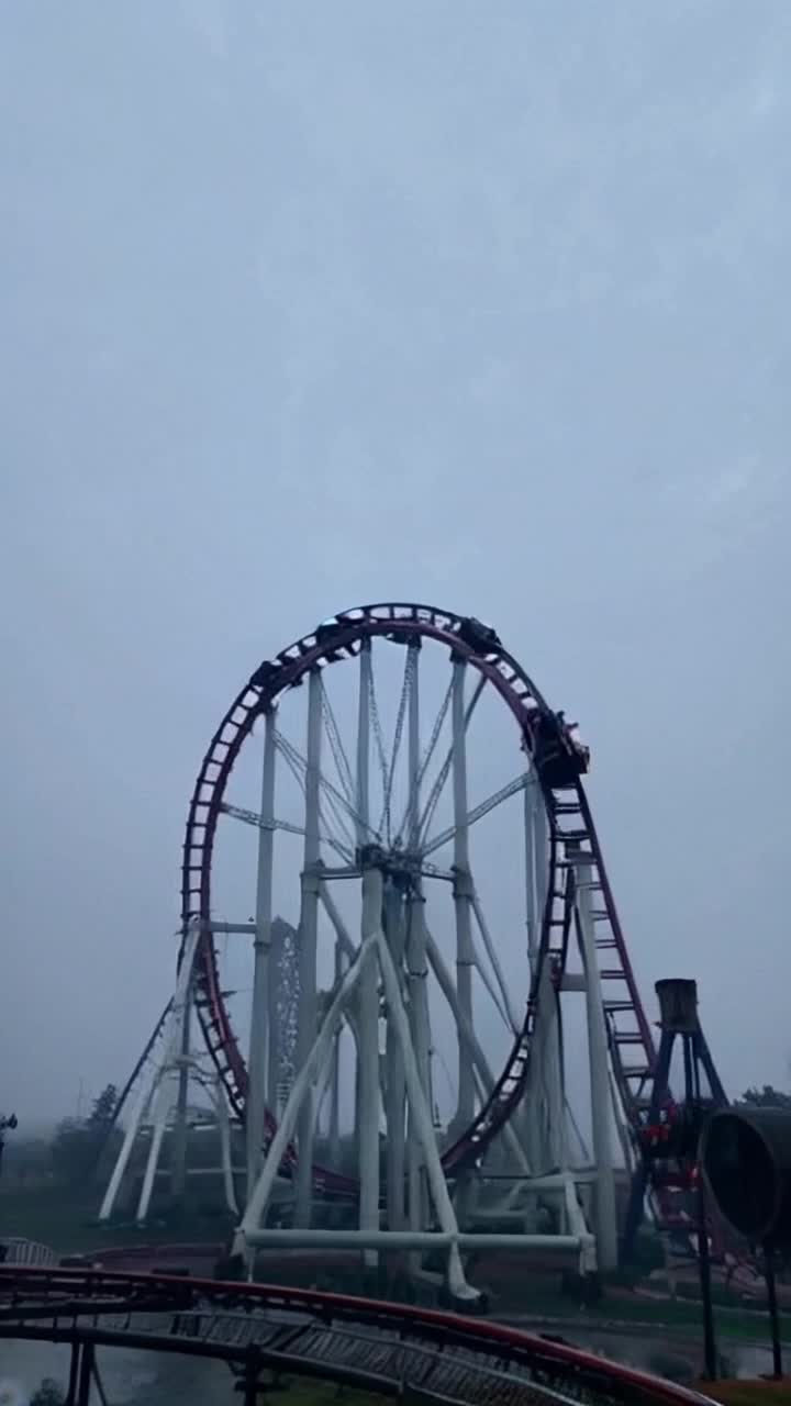 Towering rollercoaster twisting gracefully through the clouds with sharp drops and looping turns Thrilling cars racing along tracks screaming riders gripping their safety bars Fog swirling ominously beneath the ride as dim lights flicker through a dense gray mist creating an eerie atmosphere high above an abandoned amusement park
