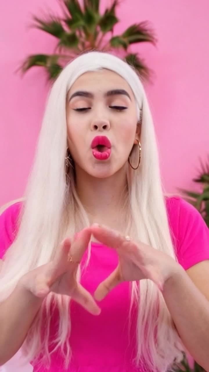 Latina girl in her 20s with long white hair beatboxing, wearing big thick hoop earrings, pink clothes, pink background, palm trees in the background