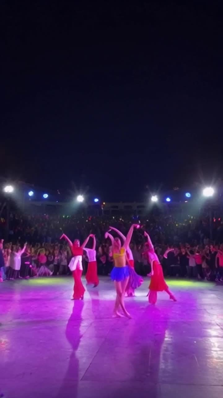 Graceful dancers twirling in colorful costumes radiating energy, bodies moving in sync with vibrant beats flowing through the air, illuminated by shimmering lights reflecting off the polished floor, backdrop of an energetic crowd cheering and clapping, electric atmosphere pulsing with life, slow motion captures each intricate movement, closeups show expressions of joy and passion, vibrant colors swirling around, spotlight illuminating a lone dancer performing a breathtaking leap, shadows dancing along the walls, captivating rhythm surrounding the scene creating an immersive experience of joy and artistic expression