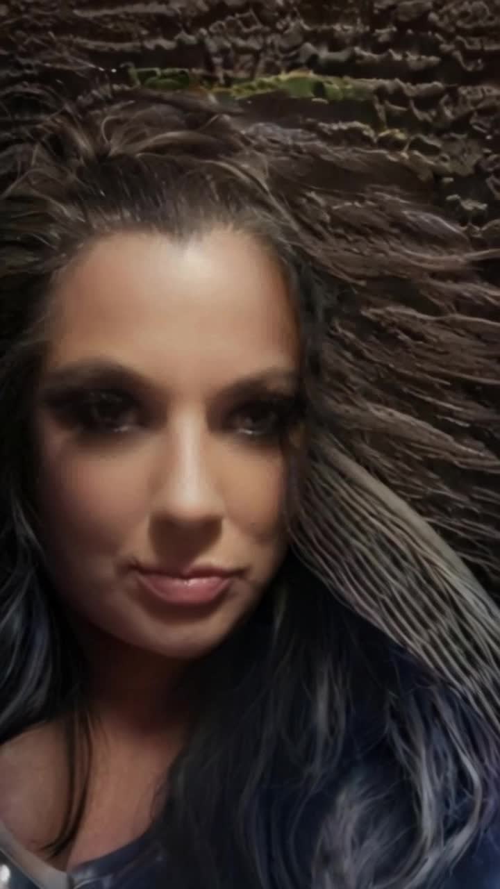 This Graceful woman with cascading ebony hair adorned in sleek black leather catsuit gliding effortlessly through urban alleyway illuminated by flickering neon lights reflecting off rainsoaked pavement