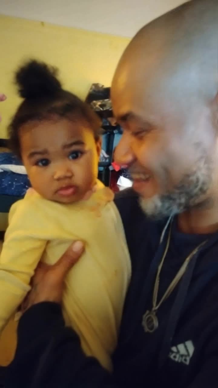 Joyful father cradling infant daughter both beaming with delight exchanging playful glances cozy couch enveloped in soft sunlight colorful cushions scattered around walls adorned with cheerful family photos gentle music playing in the background creating a warm and inviting atmosphere