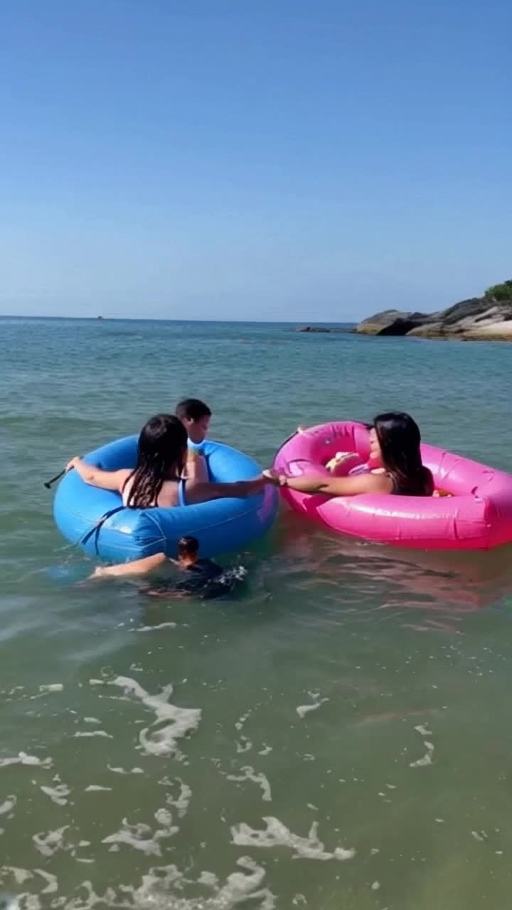 Mother and toddler daughter hold on to opposite sides of an inflatable beach raft , as they relax in the gentle waves they are startled by the sudden appearance of a dark head popping out of the water next to them  The sun is shining and their humorous surprise is comical