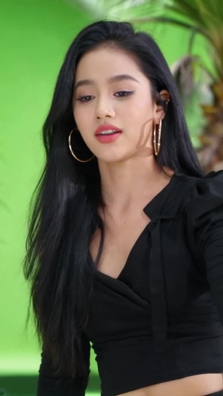 Latina girl in her 20s with long black hair rapping, wearing big thick hoop earrings, black clothes, bright green background, palm trees in the background