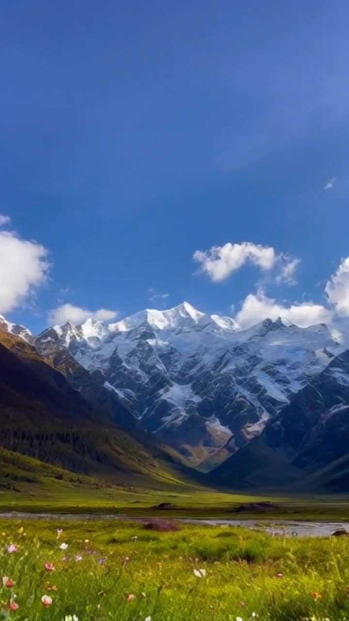 Majestic peaks adorned with snow glistening under a bright sun dramatic clouds slowly drifting across deep blue skies tranquil valleys blanketed in vibrant green lush wildflowers swaying gently in a warm breeze