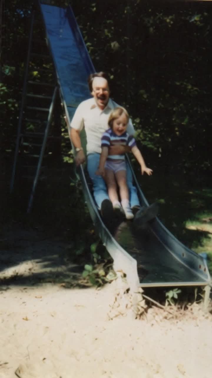 Joyful father with sparkling eyes daughter with shining smile perched atop gleaming metal slide embracing thrill of adventure gliding down with carefree laughter faces illuminated by pure excitement spiraling through air radiating happiness echoes of giggles bouncing around vibrant playground colorful equipment surrounded by soft grass swirling leaves sunlight filtering through majestic trees inviting playful children to join in the fun