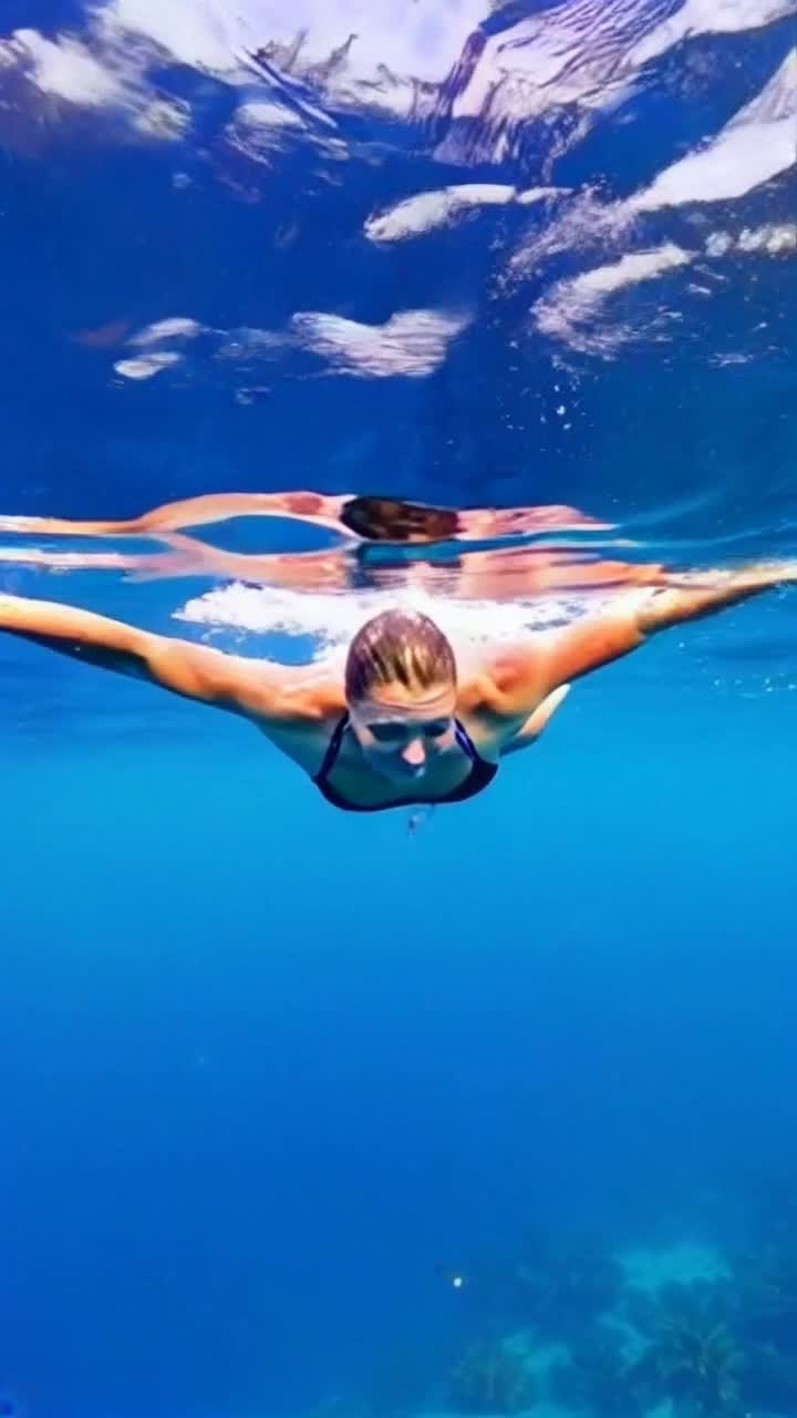 Jenna radiates strength with determination shining in her eyes, a graceful warrior embracing her journey. She plunges fearlessly into waves, arms slicing through water like a confident dancer. Sunlight sparkles on the surface, illuminating her path as vibrant marine life flits beneath. Gentle whispers of ocean breeze and rhythmic waves create a symphony of serenity, inspiring her relentless spirit. Lush coastal landscape frames the scene, palm trees swaying in harmony with her empowered resolve. Each stroke through the crystal-clear water fuels her transformation, connecting body and soul in a celebration of resilience and self-discovery