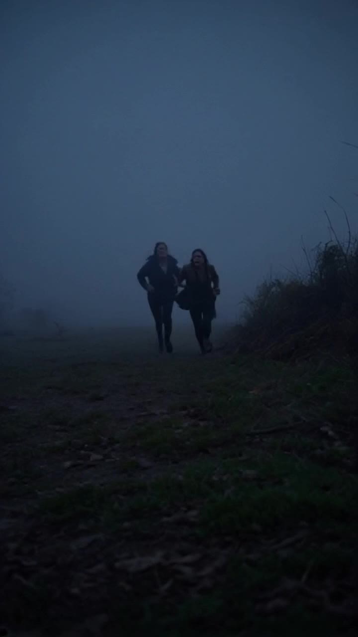 Two women scared running away from the camera, dark and foggy scene, horror themed atmosphere 
