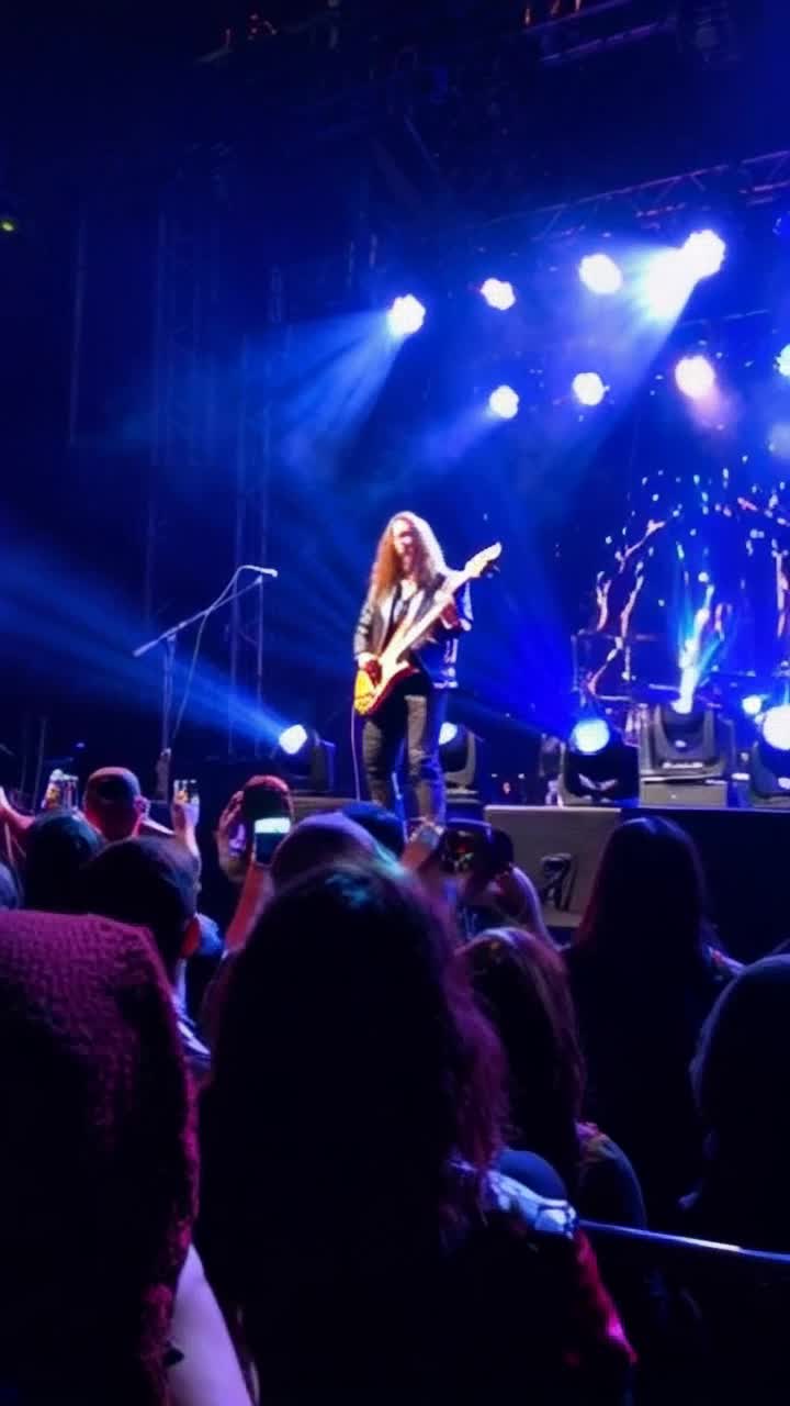 Charismatic heavy metal star with long flowing hair and leather jacket strumming electric guitar passionately on stage unleashing raw energy Bright colorful lights flashing and pulsating in sync with thunderous crowd cheering against a backdrop of roaring amplifiers and smoky atmosphere creating an electrifying concert scene