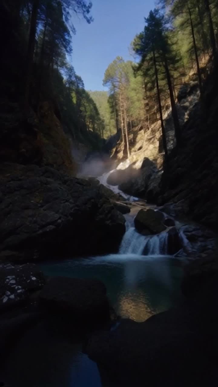 Phosphorescent water pours out of a mountain cave, half in sunlight, half in shadow that catches beams of sunlight through forest branches in its mist rising from cool pools of water from below