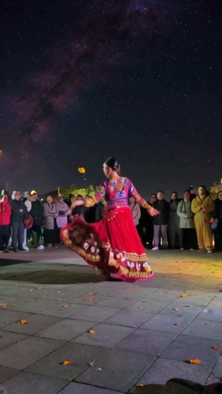 Sufi dancer  in flowing vibrant attire spins gracefully in mesmerizing rhythm surrounded by a circle of devotees entranced by the performance under a starry night sky vibrant with colorful lights illuminating the atmosphere traditional instruments play softly enhancing the spiritual ambiance as fragrant marigold flowers cascade from above creating a magical aura amidst the festive spirit of Navratri