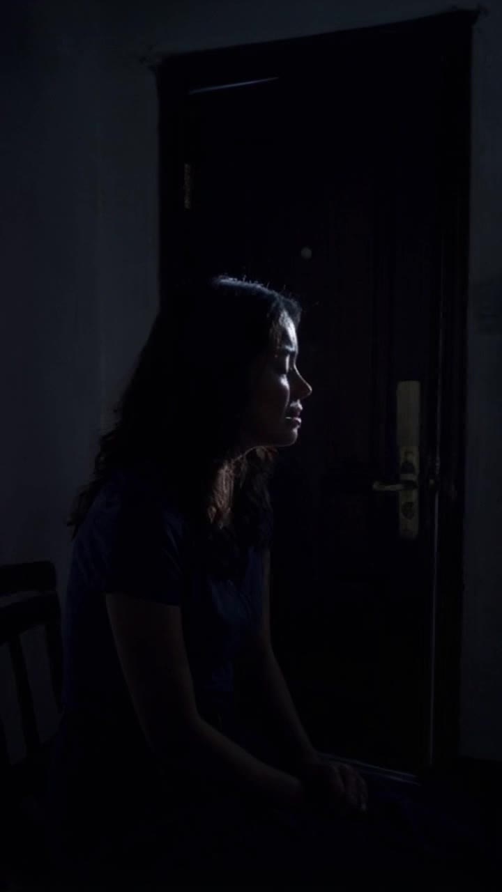 In a dimly lit, shadowy room, Sharmila sits alone, crying softly with tears streaming down her face Suddenly, the door bursts open with a loud thud, and Viransh enters dramatically, his silhouette framed against the doorway The scene is intense and emotional, with a dark, suspenseful atmosphere