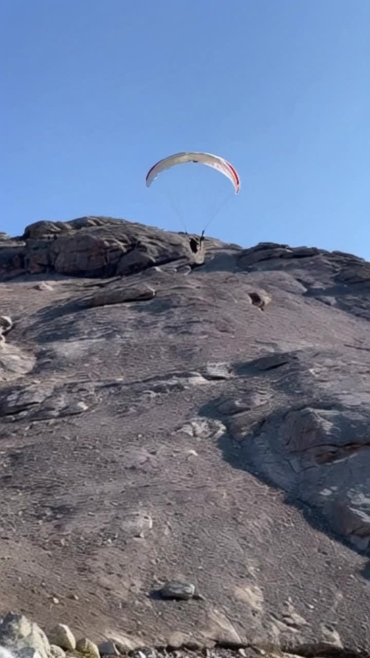 Third person view of an anthropomorphic cat paragliding down the slope of a rocky mountain closely following the approaching terrain and navigating just enough to avoid any collisions