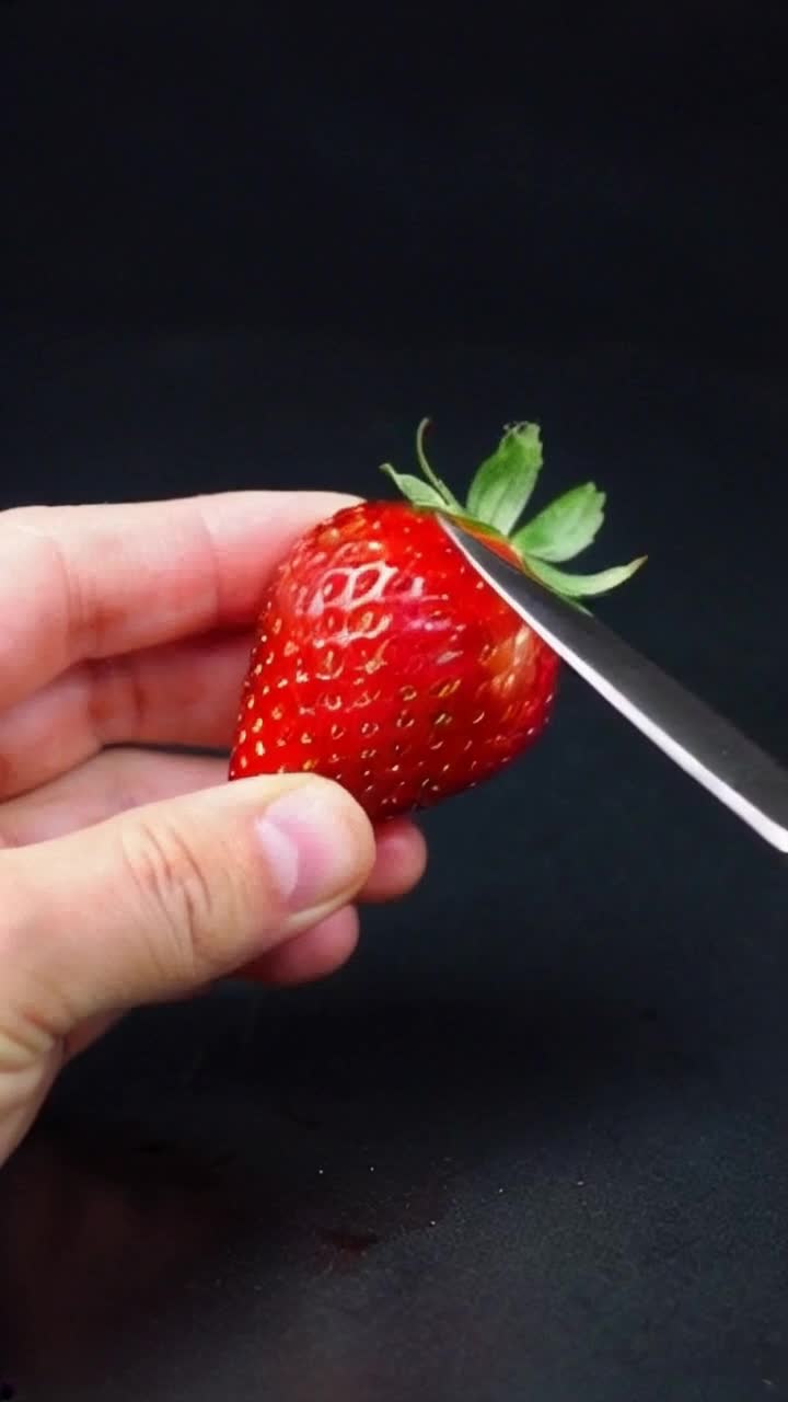 A hand holding a knife as it cuts through a strawberry made of glass
