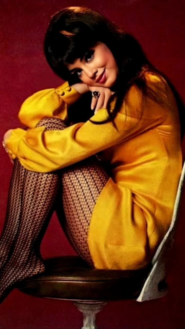 Elegant graceful woman in her 60s draped across a vibrant retro chair showcasing vintage patterns radiating confidence posing with a soft smile her hair styled in classic waves capturing timeless beauty reflecting warmth and sophistication bold colors enveloping her rich textures creating a cozy inviting atmosphere soft light filtering through a nearby window illuminating her serene expression and highlighting intricate details of the chair vivid art on walls surrounding her enhancing nostalgic charm inviting viewers to step into a moment of elegance and style capturing the essence of an era filled with grace and poise